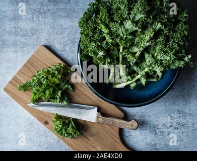 Blick von oben auf die Schüssel von Kale, Schneidebrett mit Messer und gehackten Grünkohl. Stockfoto