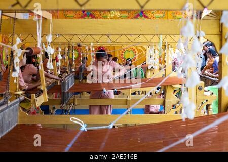 Ausstellung von Weberinnen weben Safranroben für buddhistische Mönche in einem Tempel während einer jährlichen Buddhistischen Urlaub in Mandalay, Myanmar (Birma) Stockfoto