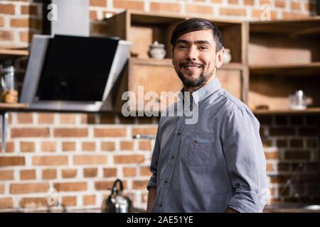 Taille von fröhlicher junger Mann, der in der Küche Stockfoto