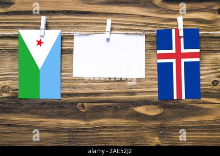 Hängenden Flaggen von Dschibuti und Island zu Seil mit wäscheklammer mit Kopie Raum befestigt auf weißem Papier auf Holz- Hintergrund. Diplomatische Beziehungen Stockfoto