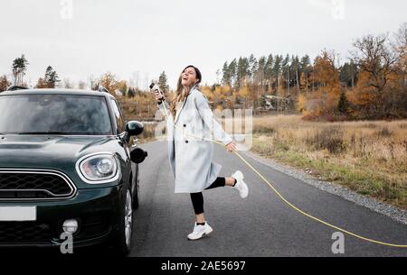 Frau tanzen spielerisch beim Einstecken in ein elektrisches Auto Stockfoto