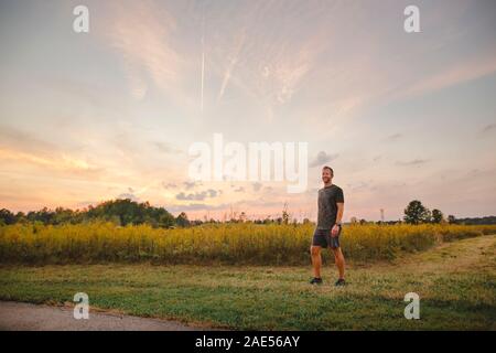 Ein stolzer Mann steht am Rand des goldenen Feld gegen den blauen Himmel bei Sonnenuntergang Stockfoto