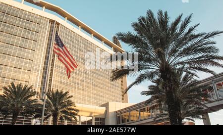 ORLANDO, Florida - Nov 11, 2019: Advent Gesundheit Krankenhaus Hauptgebäude bei Sonnenuntergang mit amerikanischer Flagge und Palmen. Stockfoto