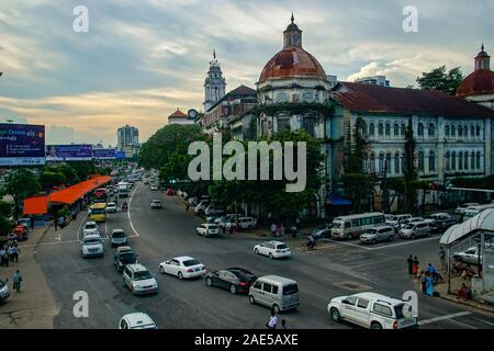 Blick über den belebten Kreuzung der Pansodan St und Strand Rd in Yangon (früher Rangoon), Myanmar (Burma) in der Dämmerung mit Verkehr und verfallenden Kolonialbauten Stockfoto