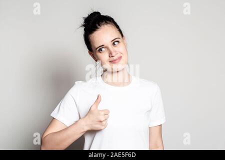 Junge Frau zeigt mit Daumen hoch, lächeln süß und gut - sieht Naturedly an jemand. Positive Emotionen. Konzept der Genehmigung. Stockfoto