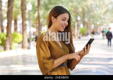 Gerne fröhliche junge Frau Tippen mit dem Finger auf Smart Phone auf Platz der Stadt. Stockfoto