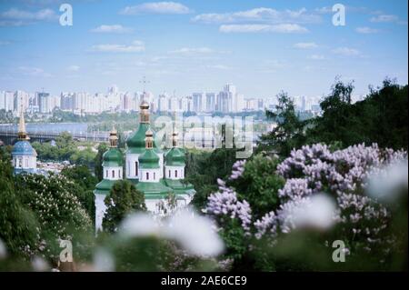 Feder Kiew Panorama. Kirche, blühender Flieder in der Ukraine. Blick auf die Stadt und den Fluss Dnepr, Vydubychi Kloster. Kiew Landschaften Stockfoto