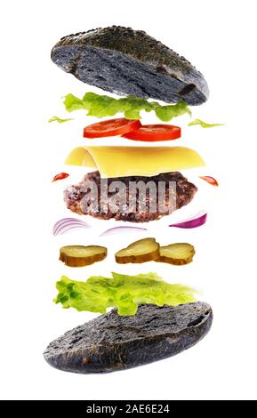 Lecker Hamburger mit Brot von schwarzer Farbe auf weißem Hintergrund. Frisch gebackene Burger mit fliegenden Zutaten Stockfoto