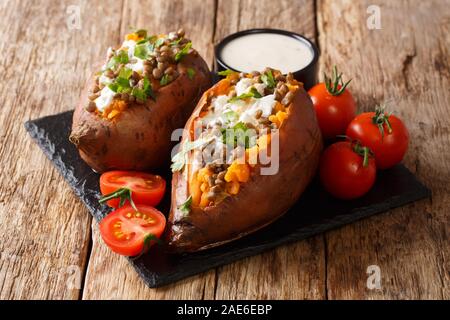 Landhausstil gebackene Kartoffel mit Linsen, Knoblauch und Petersilie gefüllt serviert mit saurer Sahne closeup auf eine Schiefertafel auf dem Tisch. Horizontale Stockfoto