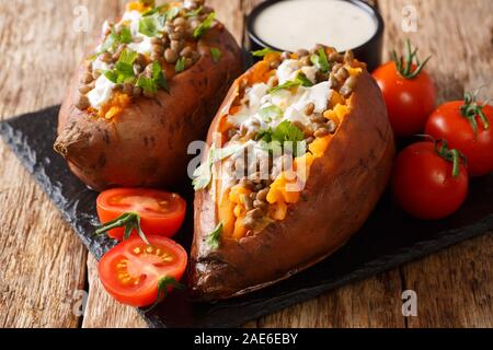 Organisches ganzes gebackene Kartoffel mit Linsen, Knoblauch und Petersilie serviert mit saurer Sahne closeup auf eine Schiefertafel auf dem Tisch. Horizontale Stockfoto