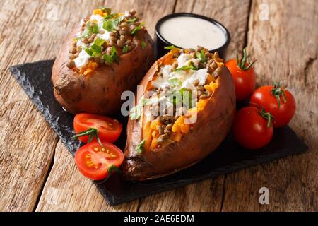 Vegetarisches Menü gebackene Kartoffel mit Linsen mit Sauerrahm und Tomaten in der Nähe serviert auf einem Schiefer Board auf dem Tisch. Horizontale Stockfoto