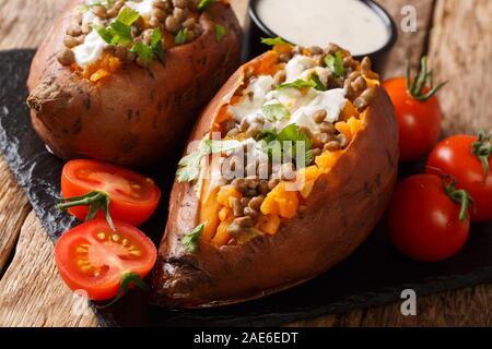 Ganze gebackene Kartoffel mit Linsen mit Sauerrahm und Tomaten in der Nähe serviert auf einem Schiefer Board auf dem Tisch. Horizontale Stockfoto