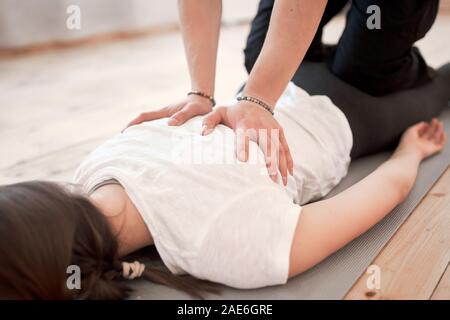 Der Mensch tut Rückenmassage von brunette liegende Frau auf grauem Teppich in der Turnhalle Stockfoto