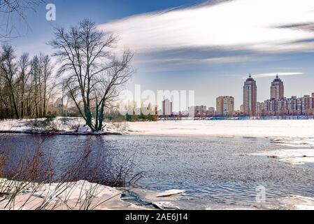 Blick auf Weiden und Pappeln in der Nähe des gefrorenen Fluss Dnepr in Kiew im Winter. Hohe Gebäude im Hintergrund. Stockfoto