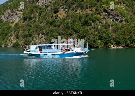 Koman, Albanien, dem 7. Juli 2019: ein Tourist Boot überholt die Autofähre auf Komani See in den Dinarischen Alpen von Albanien Stockfoto