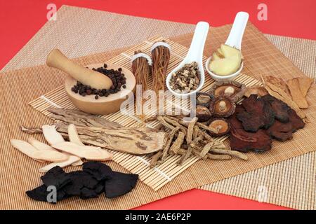 Chinesische Kräuter verwendet als Stärkungsmittel in traditionelle pflanzliche Medizin auf Bambus und roten Hintergrund. Stockfoto