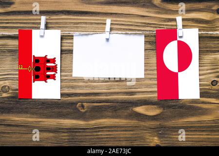 Hängenden Flaggen von Gibraltar und Grönland zu Seil mit wäscheklammer mit Kopie Raum befestigt auf weißem Papier auf Holz- Hintergrund. diplomatischen Relati Stockfoto