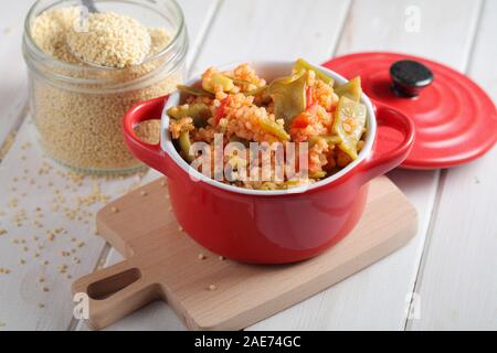 Millet Porridge mit grünen Bohnen und Tomaten in rot Teller auf einem rustikalen Tisch Stockfoto