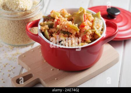 Millet Porridge mit grünen Bohnen und Tomaten in rot Teller auf einem rustikalen Tisch Stockfoto