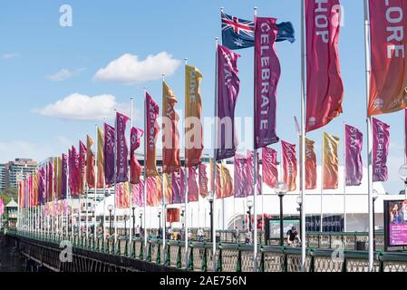 Mehrfarbige banner Fahnen flattern in einem starken morgen Wind weht über den historischen Pyrmont Bridge in Sydney's Darling Harbour-Viertel Stockfoto