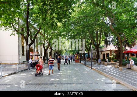 Tirana, Albanien, 8. Juli 2019: Menschen gehen an einem fussgänger Stadt Straße mit Bäumen in Tirana, Menschen in einem Café im Freien auf der Seite. Stockfoto