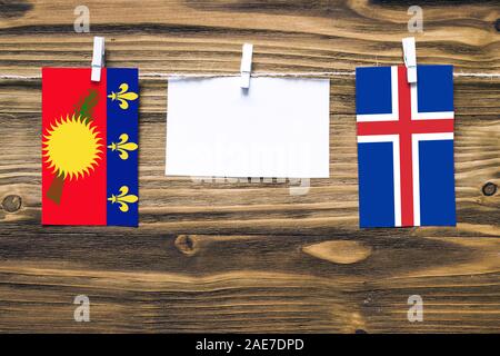 Hängenden Flaggen von Guadeloupe und Island zu Seil mit wäscheklammer mit Kopie Raum befestigt auf weißem Papier auf Holz- Hintergrund. Diplomatischen relatio Stockfoto