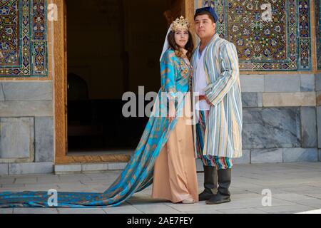 Brautpaar in traditioneller Kleidung vor der berühmten Registan Platz, Samarkand, Usbekistan, in Zentralasien posing Stockfoto