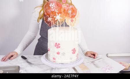 Einfügen von großen Lutscher mit Schneeflocken in den hohen Weiße, runde Kuchen als Dekoration. Stockfoto