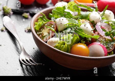 Gemüsesalat mit mocarella Käse, Salat, Tomaten, Radieschen, Gurken, Zwiebeln und Basilikum in Ton Teller Stockfoto