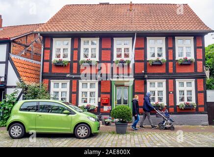 Paar mit Kinderwagen und einem grünen geparkten Auto vor dem traditionellen roten Backstein- und Holzrahmenbau in Hitzacker Niedersachsen Deutschland. Stockfoto