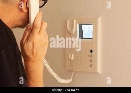 Mann Entgegennehmen eines Anrufs an einer Tür Telefon, während Sie auf dem Bildschirm auf die CRT-Bildschirm. Video Intercom Anlagen. Selektiver Fokus Bild. Stockfoto