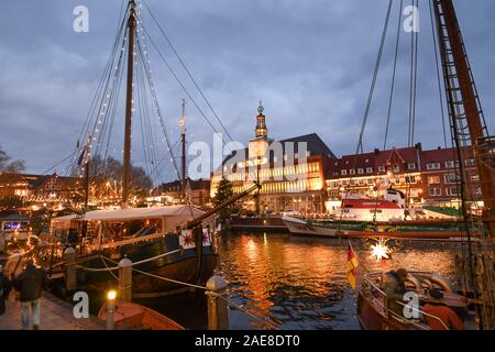 Emden, Deutschland. 07 Dez, 2019. Weihnachtliche Atmosphäre an der Emder Engelkemarkt. Besucher auf dem Weihnachtsmarkt schlendern Sie durch die festlich beleuchtete Schiffe entlang der Ratsdelft. Im Hintergrund das festlich beleuchtete Emder Rathaus. Credit: Karsten Klama/dpa/Alamy leben Nachrichten Stockfoto