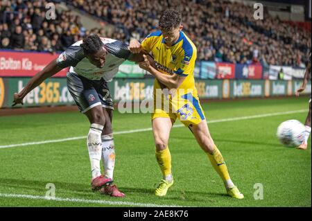 Bolton Stadium, Bolton, Großbritannien. 7 Dez, 2019. Bolton Wanderers' Joe Dodoo Verwicklung mit Wimbledon Callum Reilly während der Sky Bet Liga 1 Übereinstimmung zwischen den Bolton Wanderers und AFC Wimbledon an der Universität Bolton Stadium, Bolton am Samstag, den 7. Dezember 2019. (Credit: Ian Charles | MI Nachrichten) das Fotografieren dürfen nur für Zeitung und/oder Zeitschrift redaktionelle Zwecke verwendet werden, eine Lizenz für die gewerbliche Nutzung Kreditkarte erforderlich: MI Nachrichten & Sport/Alamy leben Nachrichten Stockfoto