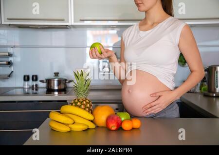 Schwangere Frau und verschiedene tropische Früchte in der Küche zu Hause Stockfoto