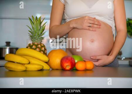 Schwangere Frau und verschiedene tropische Früchte in der Küche zu Hause Stockfoto