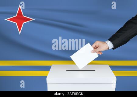 Wahl in Aruba. Die Hand des Menschen, der seine Stimme in die Wahlurne setzt. Winkte Aruba-Flagge auf Hintergrund. Stockfoto