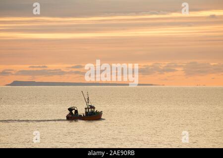 Eine Küstenfischerei Schiff, das den Hafen von Lyme Regis, heraus, in der Dämmerung an einem frostigen Morgen im Anfang Dezember 2019 verlassen hat. Die Insel Stockfoto