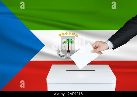 Wahl in Äquatorialguinea. Die Hand des Menschen, der seine Stimme in die Wahlurne setzt. Äquatorialguineafahne auf Hintergrund gewellt. Stockfoto