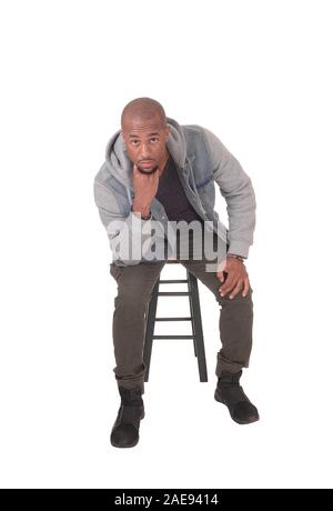 Eine junge schöne afrikanische amerikanische Mann sitzt auf einem Stuhl mit seine Finger unter das Kinn, Denken, auf weißem Hintergrund Stockfoto