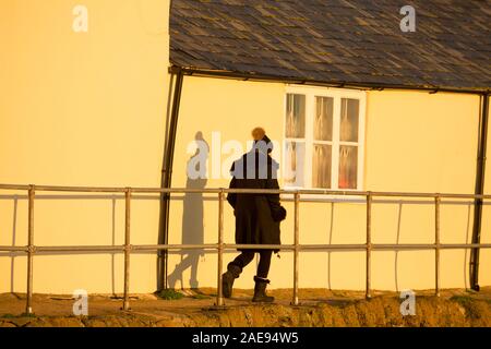 Eine Frau, die bei Sonnenaufgang an der Rückseite der Hochschule neben dem Cobb in Lyme Regis Hafen. Lyme Regis ist auf der Heritage Coast o gelegen Stockfoto
