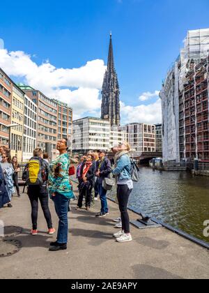 Geführte Wanderung Gruppentouristen auf einem Gehweg am Nikolaifleet-Kanal mit Blick auf historische Gebäude und die Gotische St. Nikolauskirche Hamburg Deutschland Stockfoto