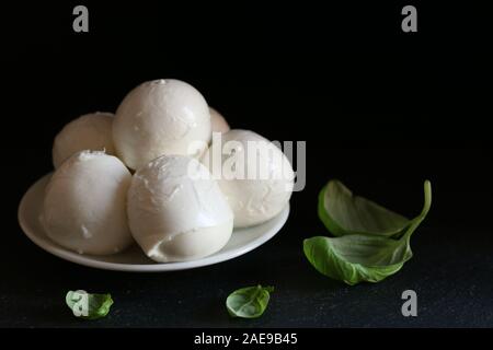Büffelmozzarella mit Basilikumblättern - frische Zutaten für Caprese-Salat mit Kopierfläche auf dunklem Hintergrund. Stockfoto