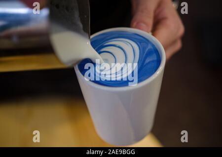 Closeup Bild der männlichen Händen gießen Milch und Vorbereitung blau Matcha Latte. Blue latte Art Stockfoto