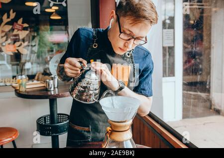 Barista Vorbereitung filter Kaffee im Freien. Junge männliche Barista gießt kochendes Wasser aus dem Wasserkocher Stockfoto