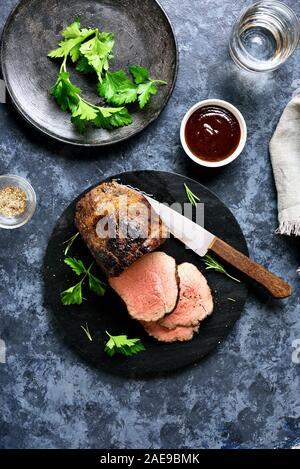 In Scheiben geschnitten gegrilltes Rindfleisch auf Holzbrett über Stein Hintergrund. Medium gebratenes Roastbeef. Ansicht von oben, flach Stockfoto