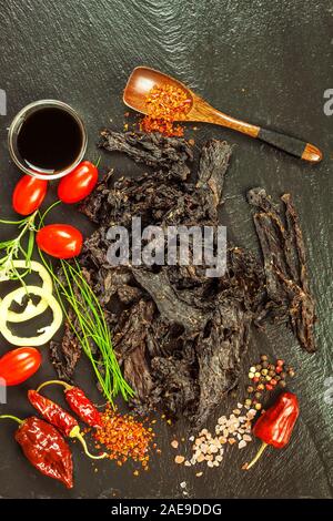 Getrocknetes Fleisch am Küchentisch. Die inländische Produktion von getrocknetem Rindfleisch. Fleisch mariniert in Chili. Diät essen. Haltbare Lebensmittel. Proteine für Sportler. Stockfoto