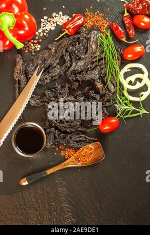 Getrocknetes Fleisch am Küchentisch. Die inländische Produktion von getrocknetem Rindfleisch. Fleisch mariniert in Chili. Diät essen. Haltbare Lebensmittel. Proteine für Sportler. Stockfoto