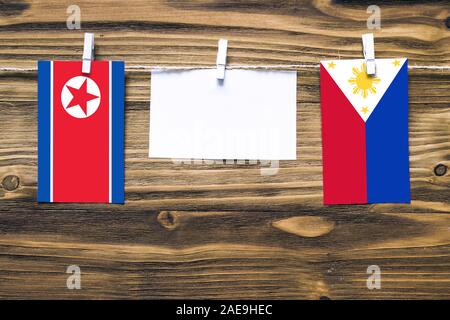 Hängende Fahnen von Nordkorea und Philippinen Seil mit wäscheklammer mit Kopie Raum auf weißem Papier auf Holz Hintergrund geklebt. Diplomatischen re Stockfoto