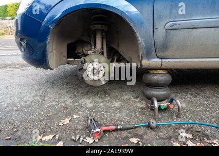 Ein Auto aufgebockt auf den Straßenrand mit eines der Vorderräder Fehlen einer Reifenpanne wird durch eine mobile Reifen reparieren Unternehmen repariert. Stockfoto