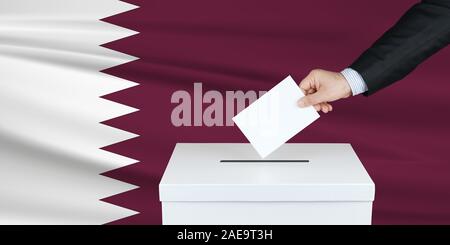 Wahl in Katar. Die Hand des Menschen, der seine Stimme in die Wahlurne setzt. Gewellte Katar-Flagge auf Hintergrund. Stockfoto